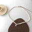 Elegant dual-tone pearl necklace with a vintage charm pendant displayed on a minimalist background.