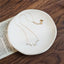Delicate baroque pearl necklace on a gold chain laid out on a ceramic plate.